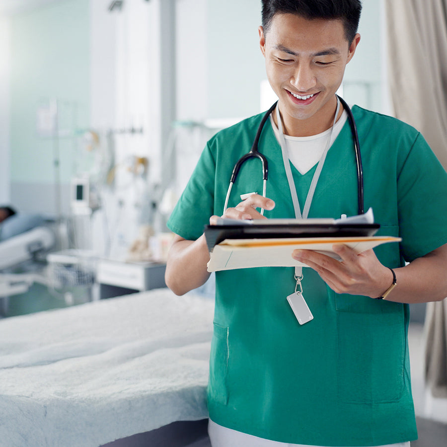 Doctor in green scrubs holding a tablet in a hospital room with an nfc keychain as lanyard