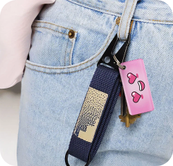 Close-up of denim jeans with a pink heart-eyes NFC keychain attached to the jeans
