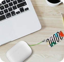 Laptop and wireless earphones case with a colorful NFC keychain attached to the case on a wooden desk